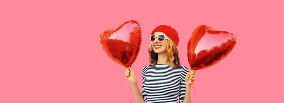 Cute portrait of happy cheerful smiling young woman with red heart shaped balloon wearing french beret hat on pink studio background