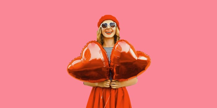 Cute portrait of happy cheerful smiling young woman with red heart shaped balloon wearing french beret hat on pink studio background