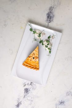 A delicious slice of savory meat pie with golden crust, layers of meat, veggies on a plate with sour cream and herbs.