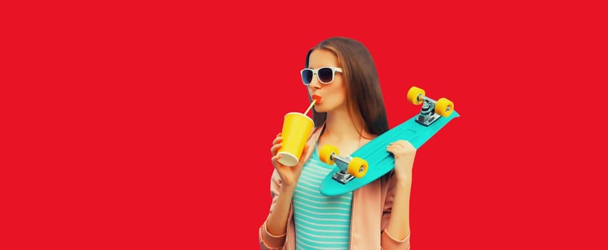 Portrait of stylish young woman with skateboard drinking juice on red background