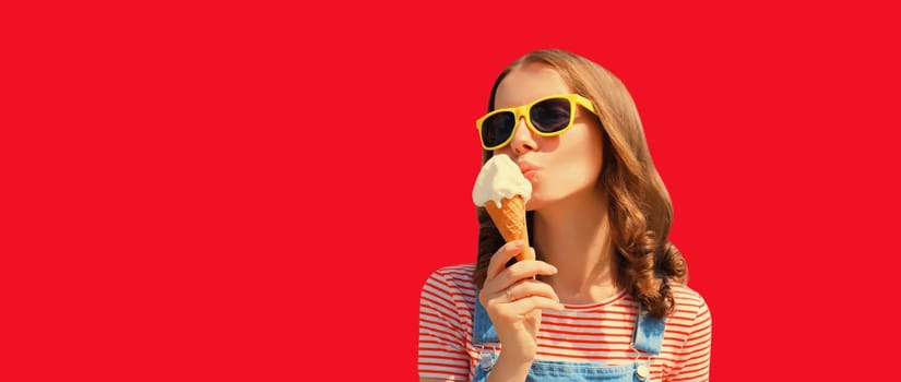 Summer portrait of happy young woman eating ice cream wearing sunglasses on red studio background