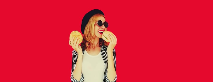 Portrait of happy cheerful young woman having fun with burger fast food isolated on red studio background