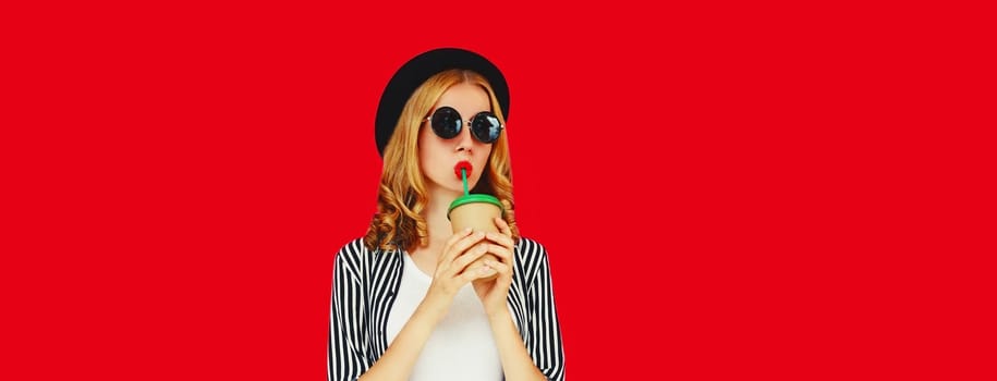 Portrait of stylish young woman drinking coffee or juice in round hat, sunglasses on red studio background