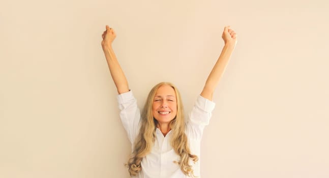 Happy lucky woman employee manager in office shirt having fun or feels victory raising her hands up at work
