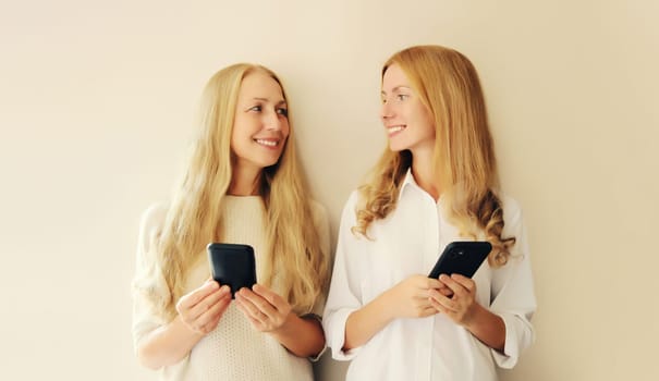 Two caucasian women with mobile phone looking at each other, middle aged mother or sister and adult daughter together on studio background