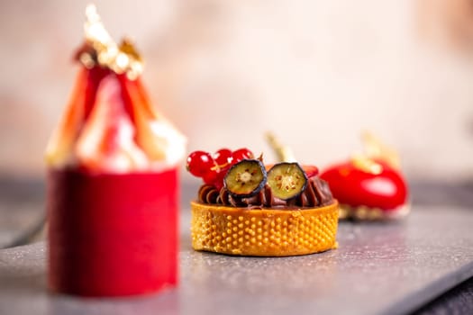 Indulgent chocolate tart, strawberry mousse, raspberry macaroon on slate board with pink background for an elegant dessert display.