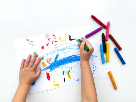 Childs hands drawing with colorful wax crayons on white paper, top view. Creative art concept for educational and developmental activities. High quality photo