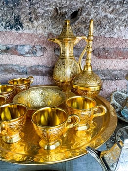 Vintage golden tea set with intricate designs on tray against rustic stone wall. Traditional ornate metalware concept for interior design and decoration. High quality photo