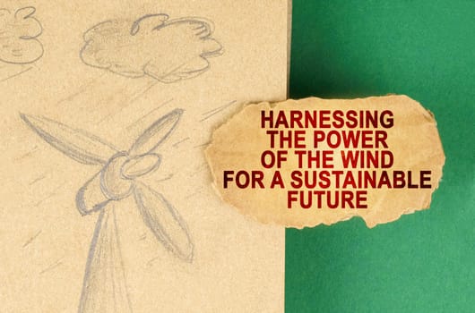 Alternative energy concept. On a green surface there is a drawing with a wind generator and a cardboard with the inscription - Harnessing the power of the wind for a sustainable future