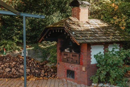 An Old Stove And Firewood For It In The Yard In The Village. Old Stone Fireplace Outdoors In The Fall. Traditional Brick Oven With Wood For Baking Bread Outdoor In Europe.