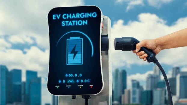 Hand pull and hold EV charger from charging station for with city horizon and sky background. Technological advancement of energy sustainability and electric power engine car using clean energy.Peruse