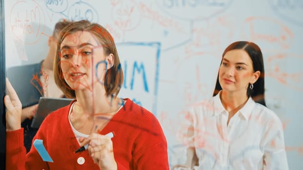 Professional business team brainstorming and working together about marketing project. Female caucasian leader writing idea on stick note while coworker present her idea confidently. Immaculate.