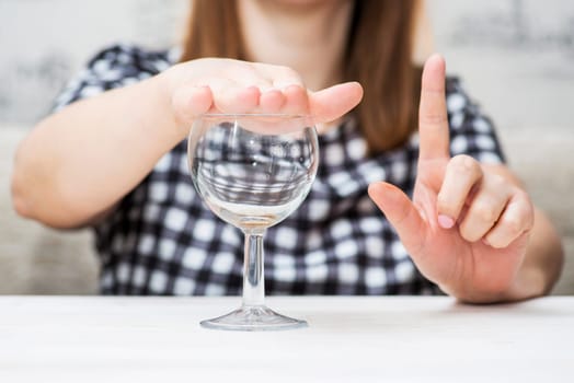 A woman's hand is shown gesturing 'no' to a glass of water, symbolizing alcohol refusal or a commitment to sobriety.