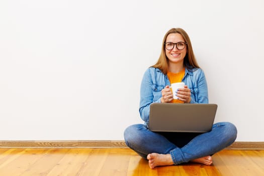 Content Woman with Laptop and Coffee Mug Sitting on Floor.