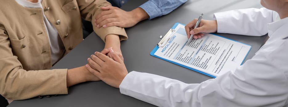 Doctor providing compassionate healthcare consultation while young couple patient holding hand, comfort each other after infertile report. Reproductive and medical fertility consulting. Neoteric