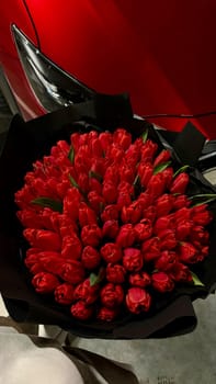 A large bouquet of bright red tulips on a red car. High quality photo