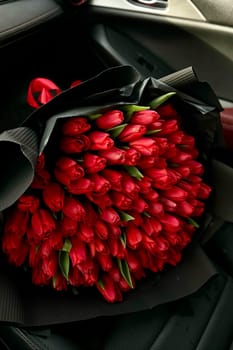 A large bouquet of bright red tulips on a red car. High quality photo