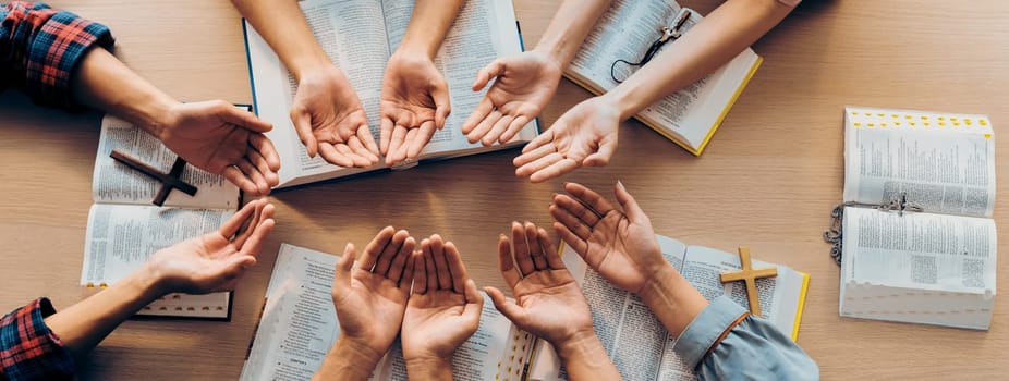 Cropped image of diversity people hand praying together at wooden church on bible book. Group of believer hold hand together faithfully. Concept of hope, religion, faith, god blessing. Burgeoning.