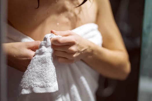 Young girl takes a shower with soap, gel, lotion, cares for her body, hygiene, woman holds a towel with her hands, close-up view.