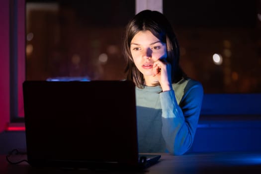 A young girl works while sitting at a laptop at night at home online, a woman is looking for information, texting, chatting using device via internet.