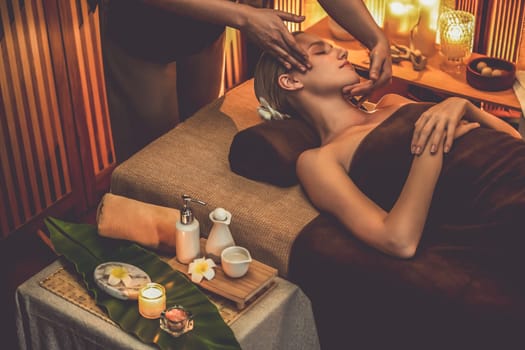 Caucasian woman enjoying relaxing anti-stress head massage and pampering facial beauty skin recreation leisure in warm candle lighting ambient salon spa in luxury resort or hotel. Quiescent