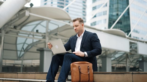 Low angle view of professional business man working on laptop at stairs. Caucasian project manager using computer to plan marketing strategy and communicate with financial team at urban city. Urbane.