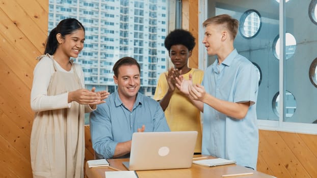 Highschool boy presenting project while teacher looking at laptop. Group of diverse student standing and explain plan while smart instructor listening and giving advise.Teamwork concept. Edification.