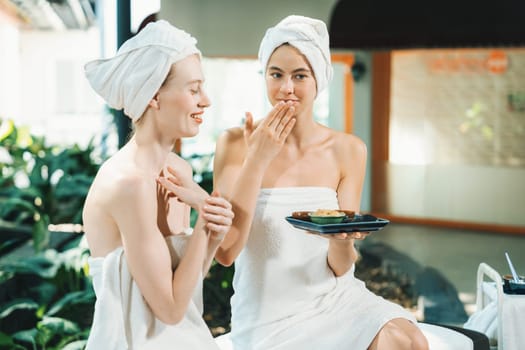 Portrait of two attractive woman in towel giggling during hold the herbal bowl surrounded by natural spa environment. Pretty girls with beautiful skin using herbal scrub at spa salon.Tranquility.