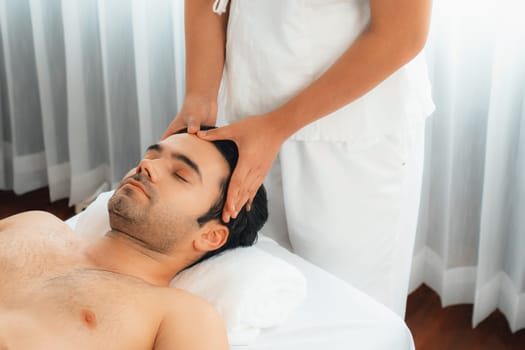 Caucasian man enjoying relaxing anti-stress head massage and pampering facial beauty skin recreation leisure in dayspa modern light ambient at luxury resort or hotel spa salon. Quiescent