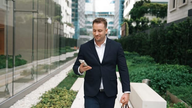 Caucasian businessman walking at park while talking to manager by using phone about planning strategy. Professional executive manager calling marketing team and sharing creative idea at city. Urbane.