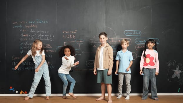 Diverse students turn around and dancing at blackboard with code or prompt at STEM technology class. Group of learners move to music and looking at camera while young boy showing thumb up. Erudition.