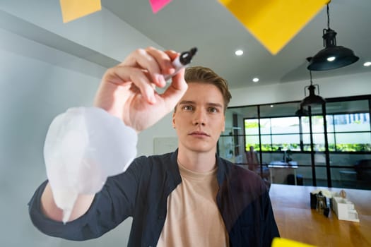 Professional caucasian businessman writing marketing idea by using mind map and sticky notes on glass board at modern meeting room. Creative business and planing concept. Closeup. Immaculate.