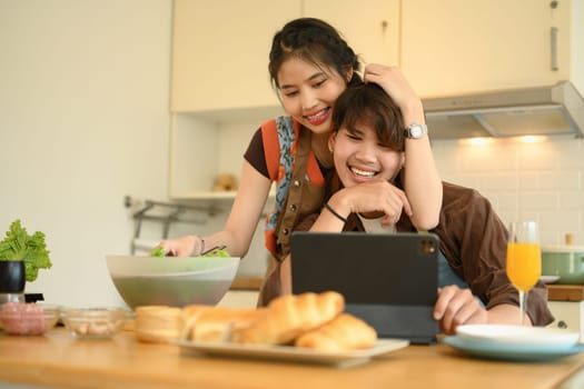 Young sweet couple reading recipe online on website while cooking healthy meal in kitchen.