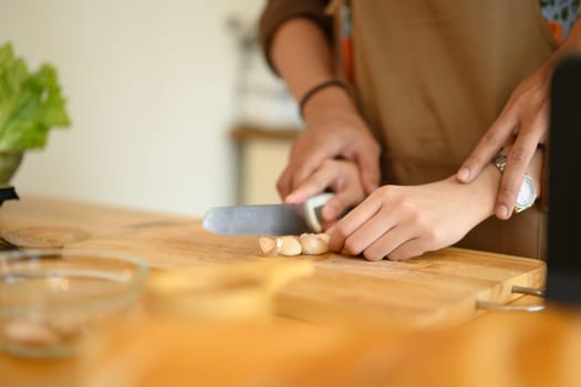 Woman hand chopping garlic on wooden board while preparing meal with her husband in the kitchen.
