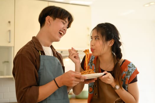 Happy young lovers eating bolognese spaghetti in kitchen. Love, relationships and food concept.