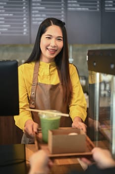 Friendly waitress serving matcha green tea and cake in a cardboard takeaway box to customer.