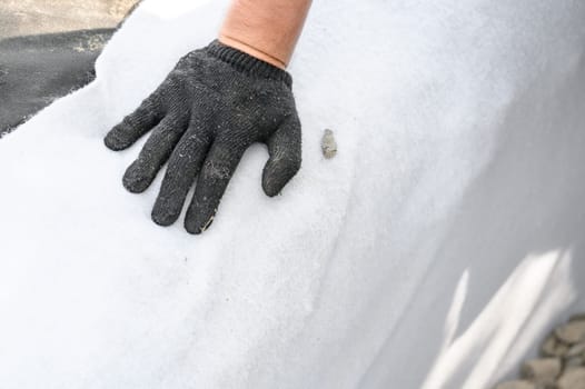The craftsman spreads white geotextile in the trench. A mans hand in black gloves on a white canvas.