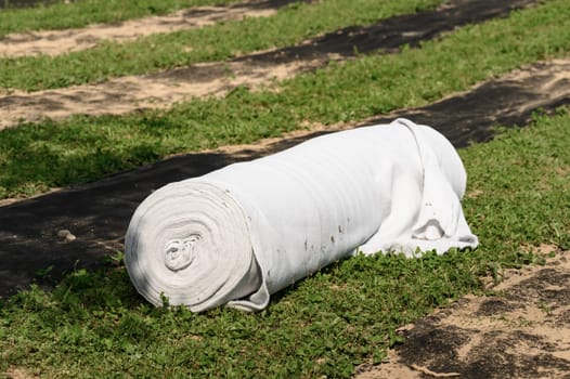 A roll of white geotextile lies on a field. Preparation for drainage works.