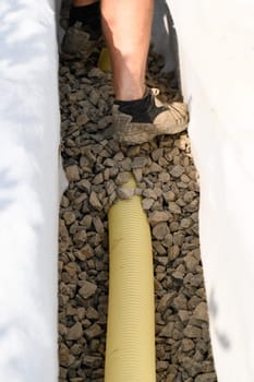 A worker stands in a drainage trench with white geotextile. Feet of the craftsman on the granite rubble close up.