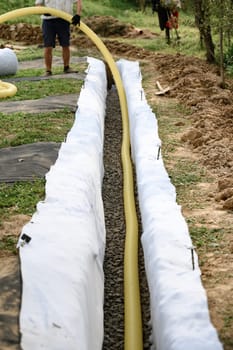 Groundwater drainage works in the field. A worker carries a yellow perforated drainage pipe.