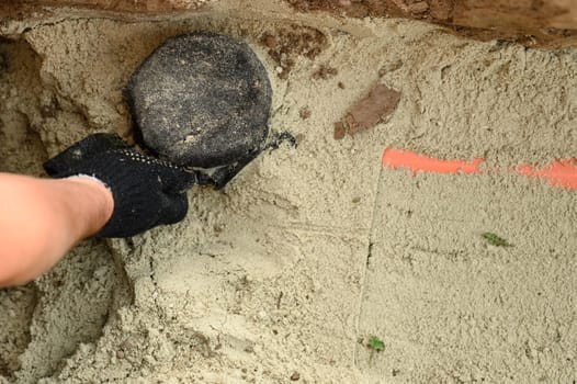 A plumber installs a reinforced orange sewer pipe during site maintenance. Hands of a plumber close-up near a sewer pipe covered with sand.