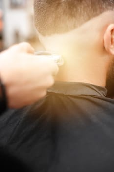 Barber shaves the temple with a cordless trimmer during a short haircut on the sides of the head.