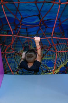 The boy climbs up the labyrinth with a web, children's activity in the playroom.
