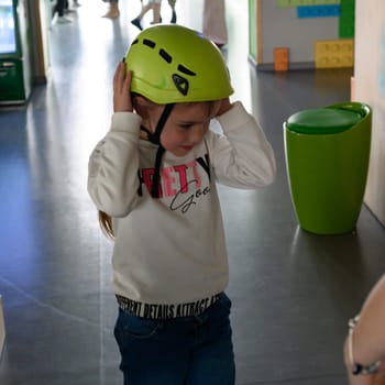 A little girl is put on a helmet as protection on the cable car, the cable car in the playroom.