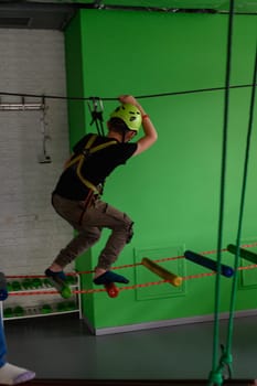 The boy is actively and attentively going through the cableway in the playroom, adrenaline and activity for children.