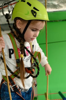 A little girl is walking on a cablewaya playroom with a cable car, a helmet and a belay is worn by a girl while running on a cable car.