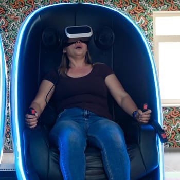 Virtual reality attraction, virtual glasses and entertainment in playrooms for children, woman wears vr glasses. A girl sits in a 5d neon chair.