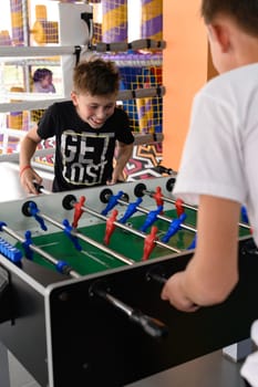 Two boys in the game room playing table football, mental and active recreation.