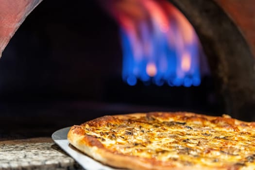 Mixed pizza fresh from the pizza oven with flames visible in the background