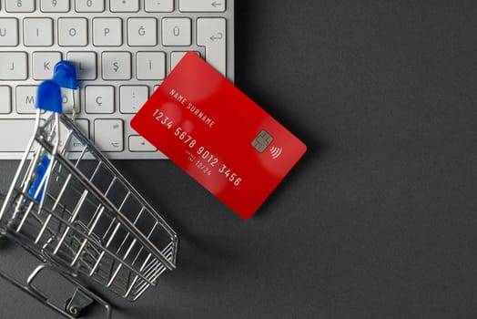 Top view of computer keyboard, credit card and mini market cart on dark gray table